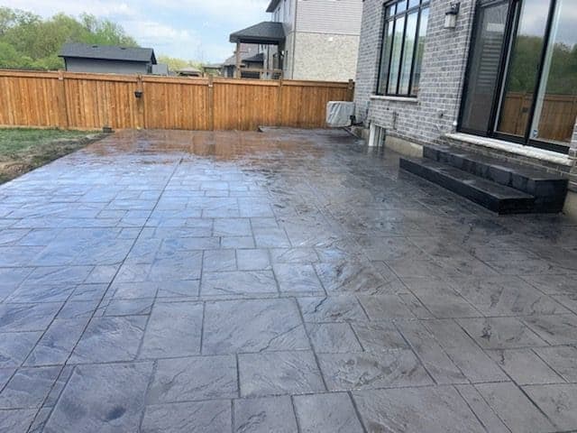 Freshly sealed grey stamped concrete patio beside a cedar fence in London, Ontario, semi-gloss finish by TriCity Concrete Sealing